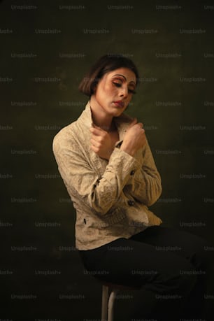 a woman sitting on a stool with her hands on her chest