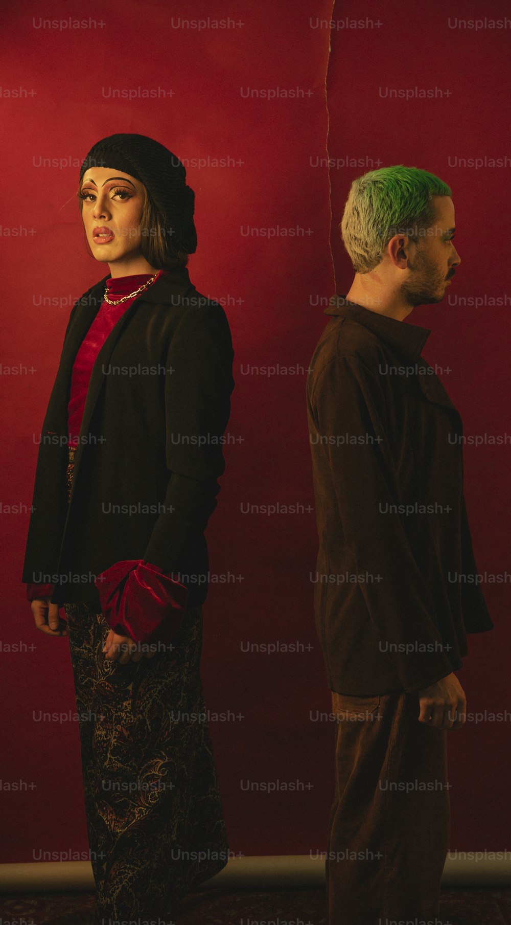 um homem e uma mulher em pé na frente de uma parede vermelha