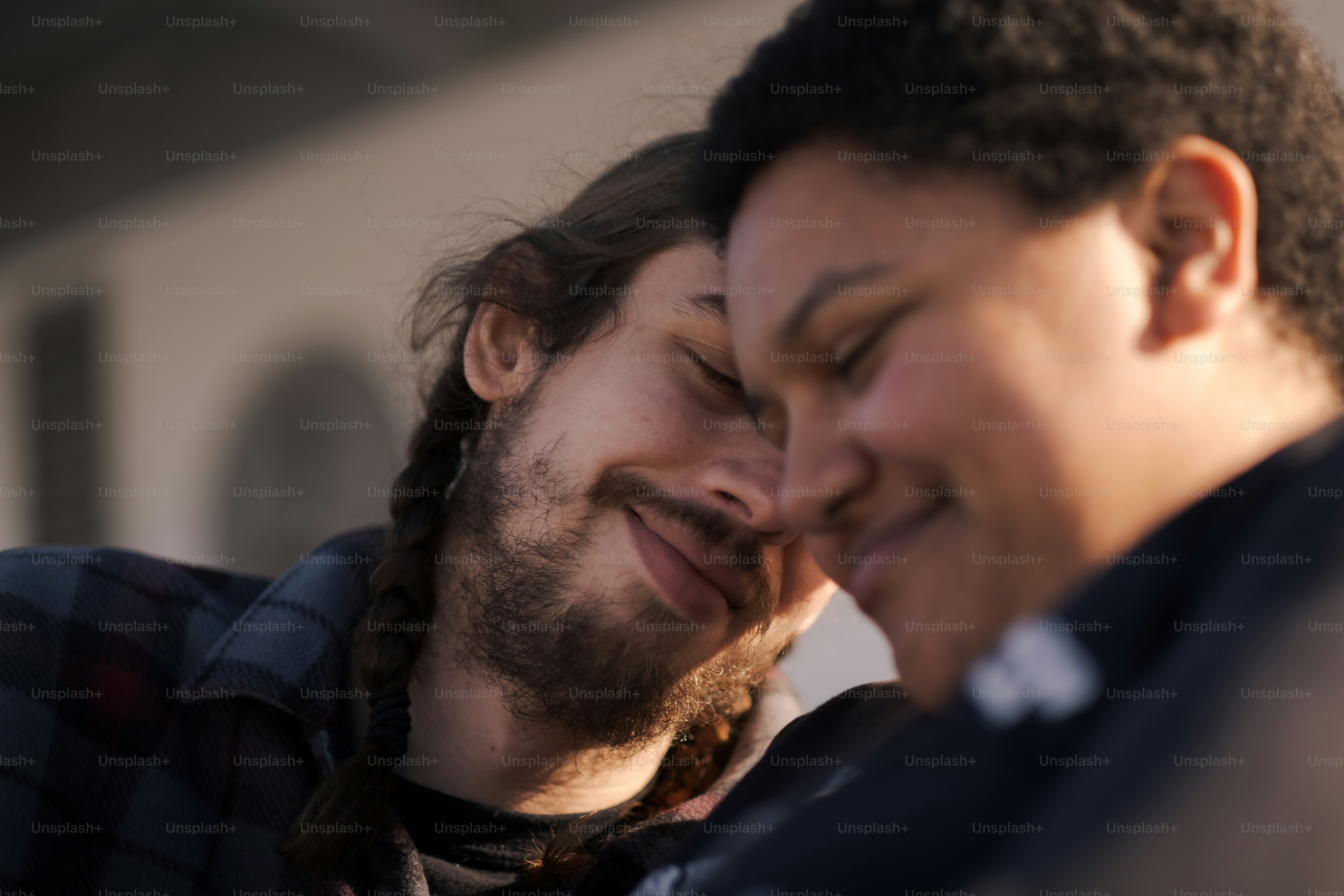 Ein Mann mit langen Haaren und Bart lächelt einen anderen Mann mit geschlossenen Augen an