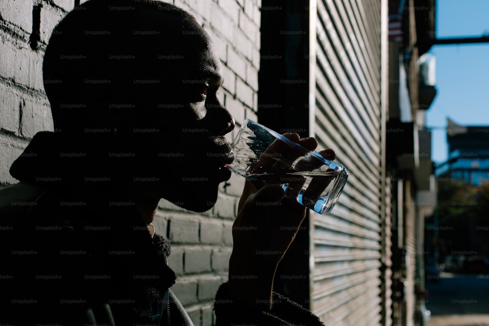 a man drinking from a glass next to a brick wall