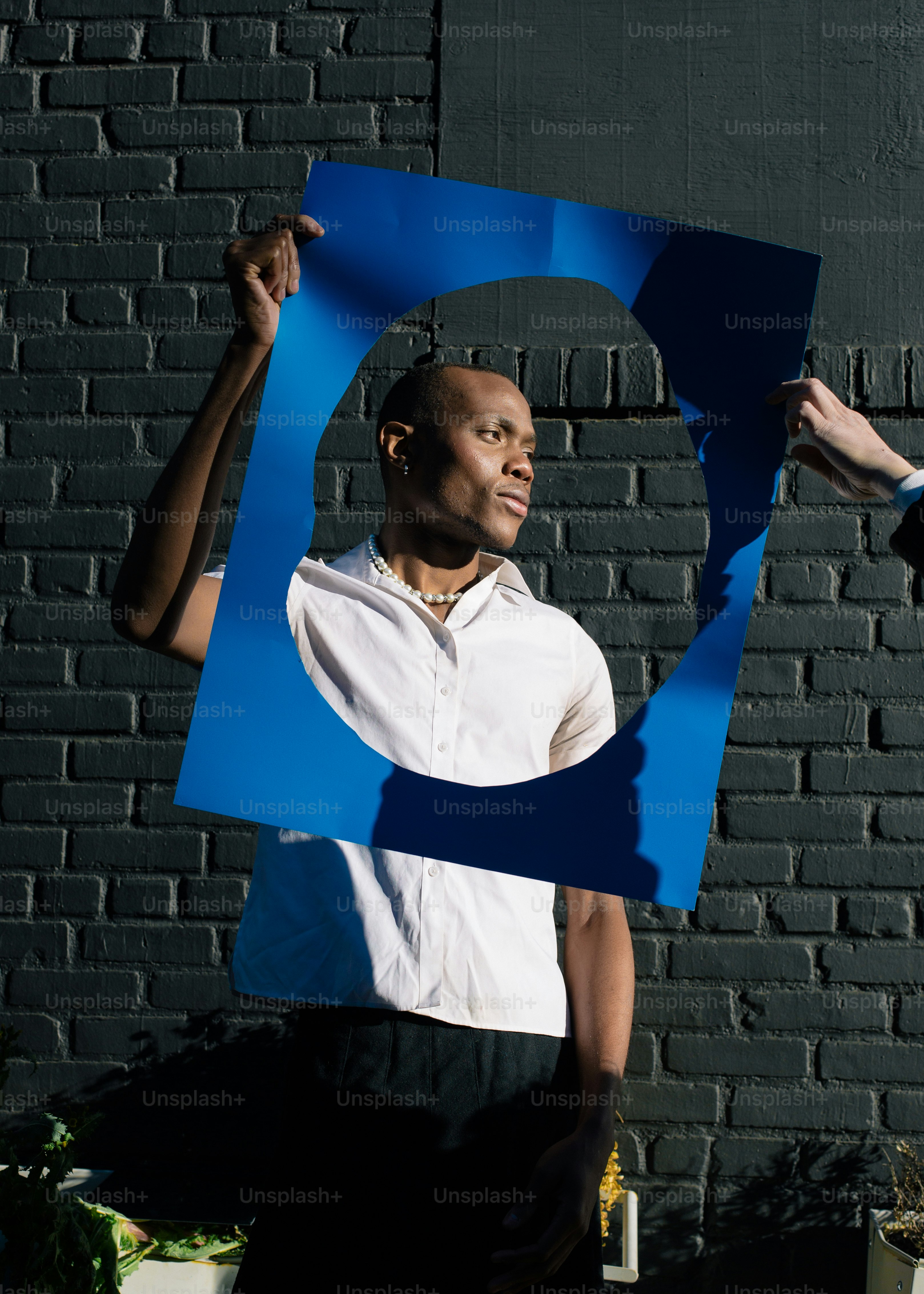 a man holding up a large blue letter in front of a brick wall