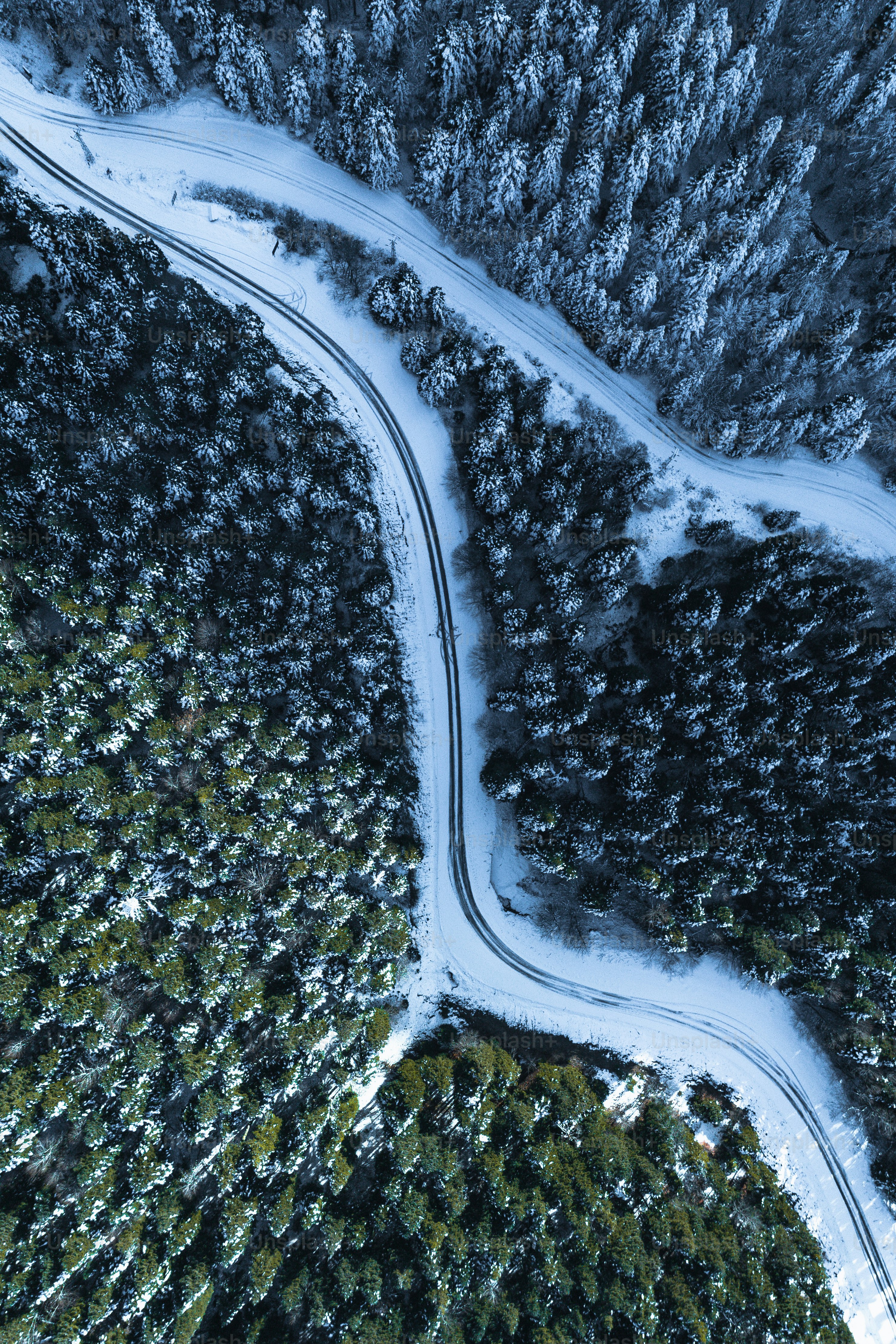 an aerial view of a road winding through a snow covered forest