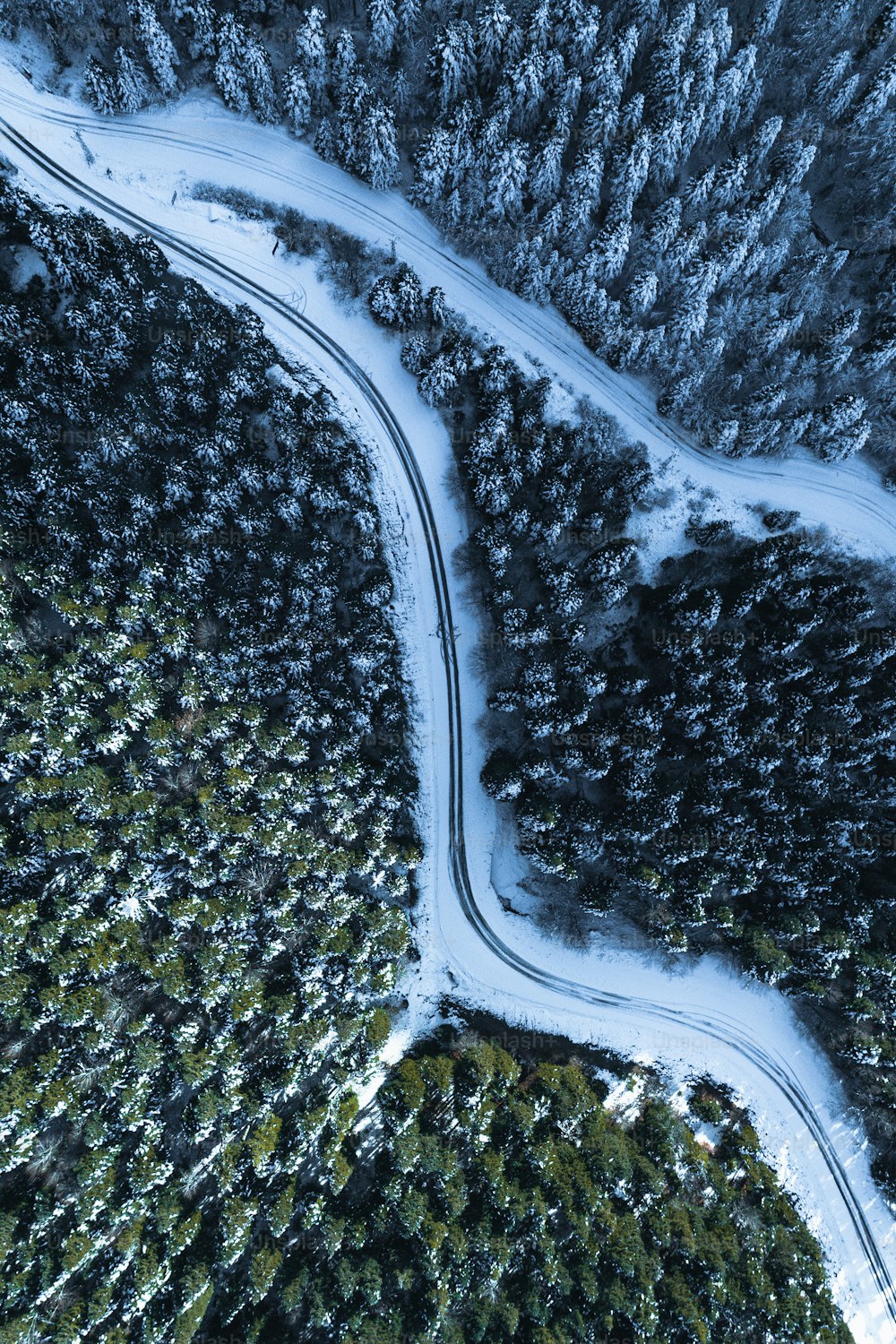 an aerial view of a road winding through a snow covered forest