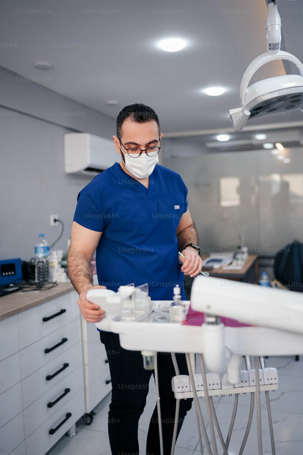 Un hombre con una camisa azul y una máscara facial parado en el consultorio de un dentista