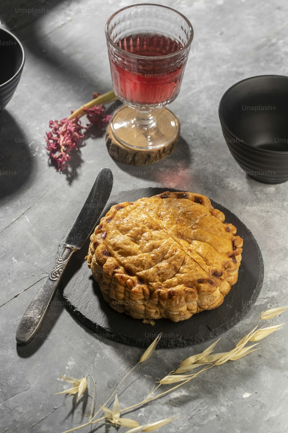 a pie sitting on top of a black plate next to a glass of wine