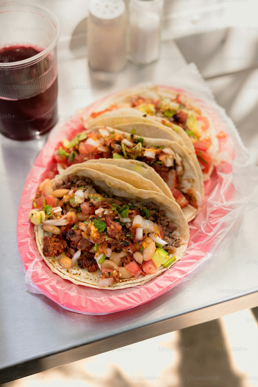 three tacos sitting on a pink plate next to a drink