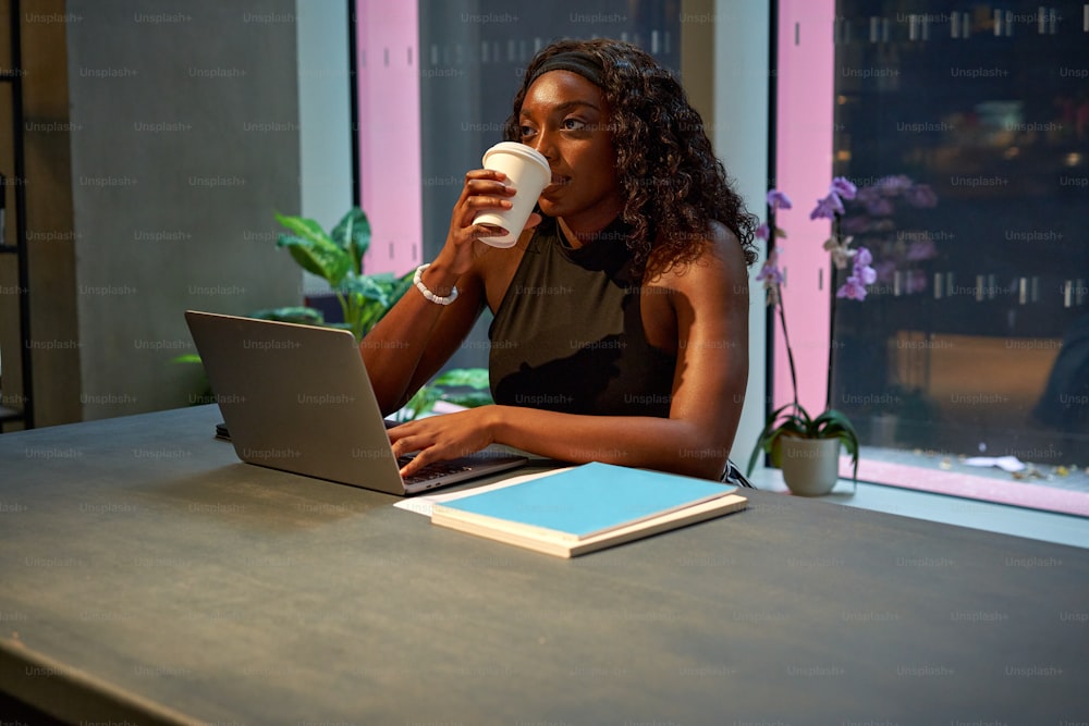 a woman sitting at a table with a laptop and a cup of coffee