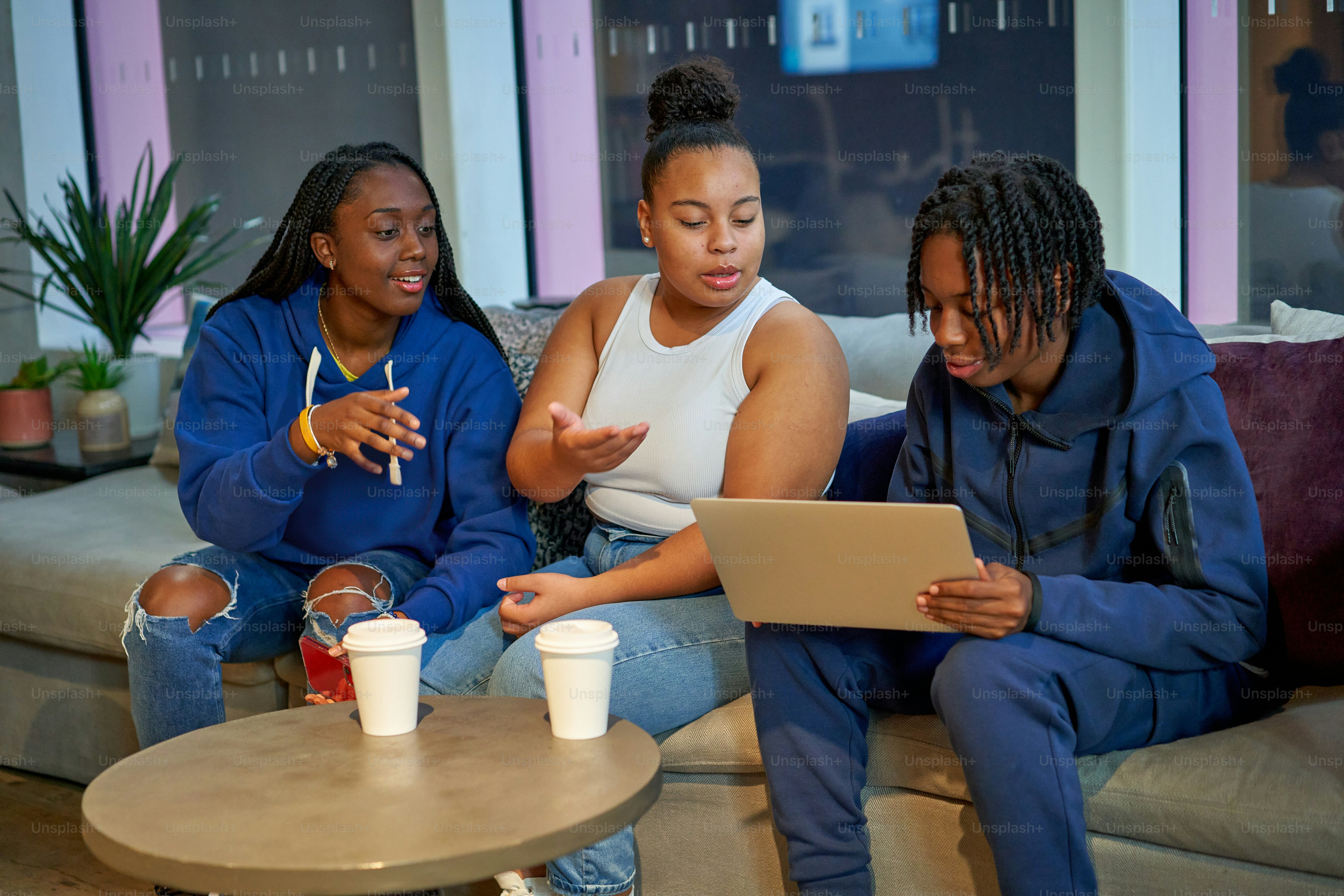 three women sitting on a couch looking at a laptop
