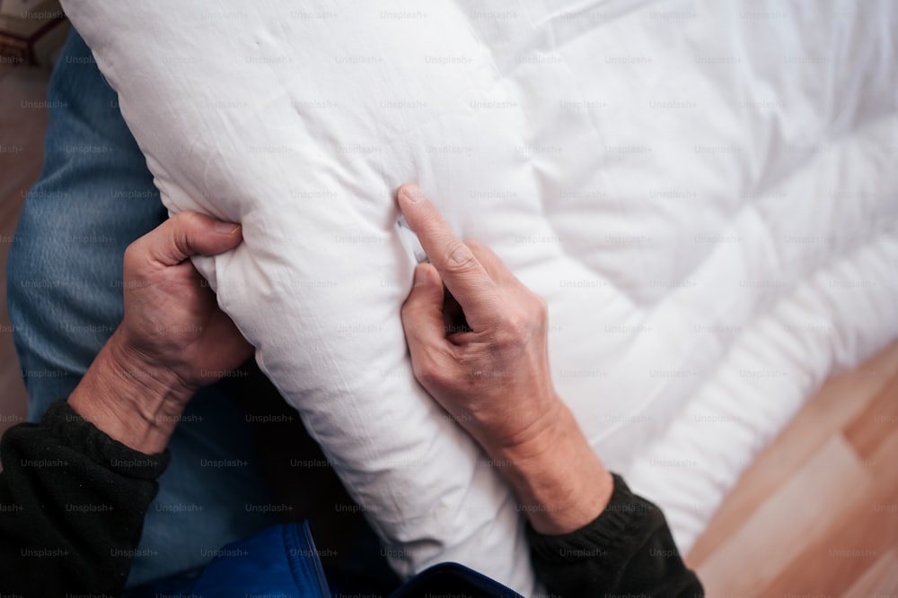 uma pessoa segurando um travesseiro em cima de uma cama
