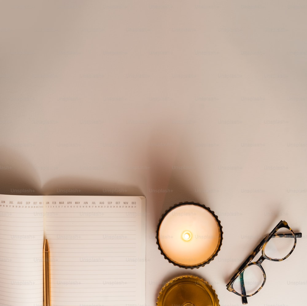 uma mesa com um caderno, caneta, óculos e uma vela