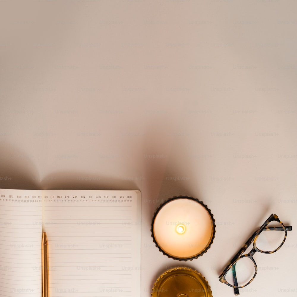 a desk with a notebook, pen, eyeglasses and a candle