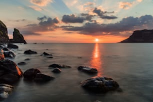 o sol está se pondo sobre o oceano com rochas em primeiro plano