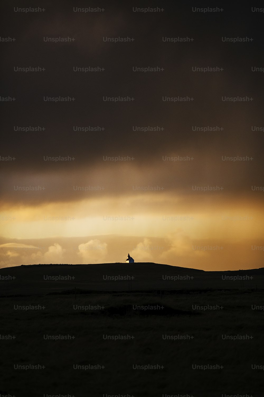 a lone horse standing on top of a hill under a cloudy sky
