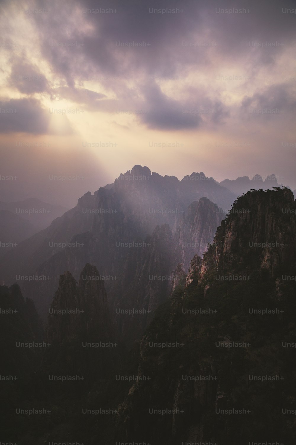 a view of a mountain range with the sun peeking through the clouds