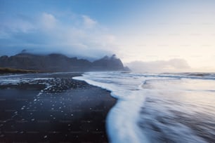 a beach with waves coming in to shore and mountains in the background