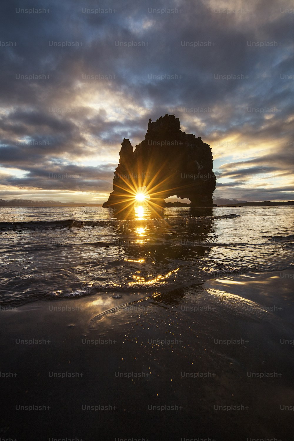 the sun is setting behind a rock in the ocean