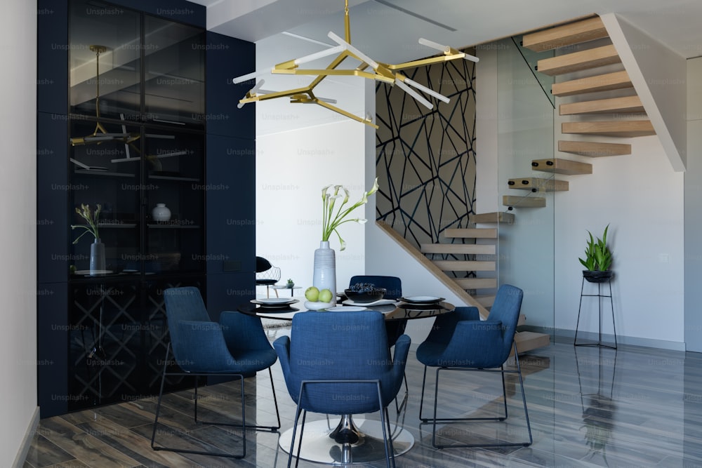 a dining room table with blue chairs and a spiral staircase