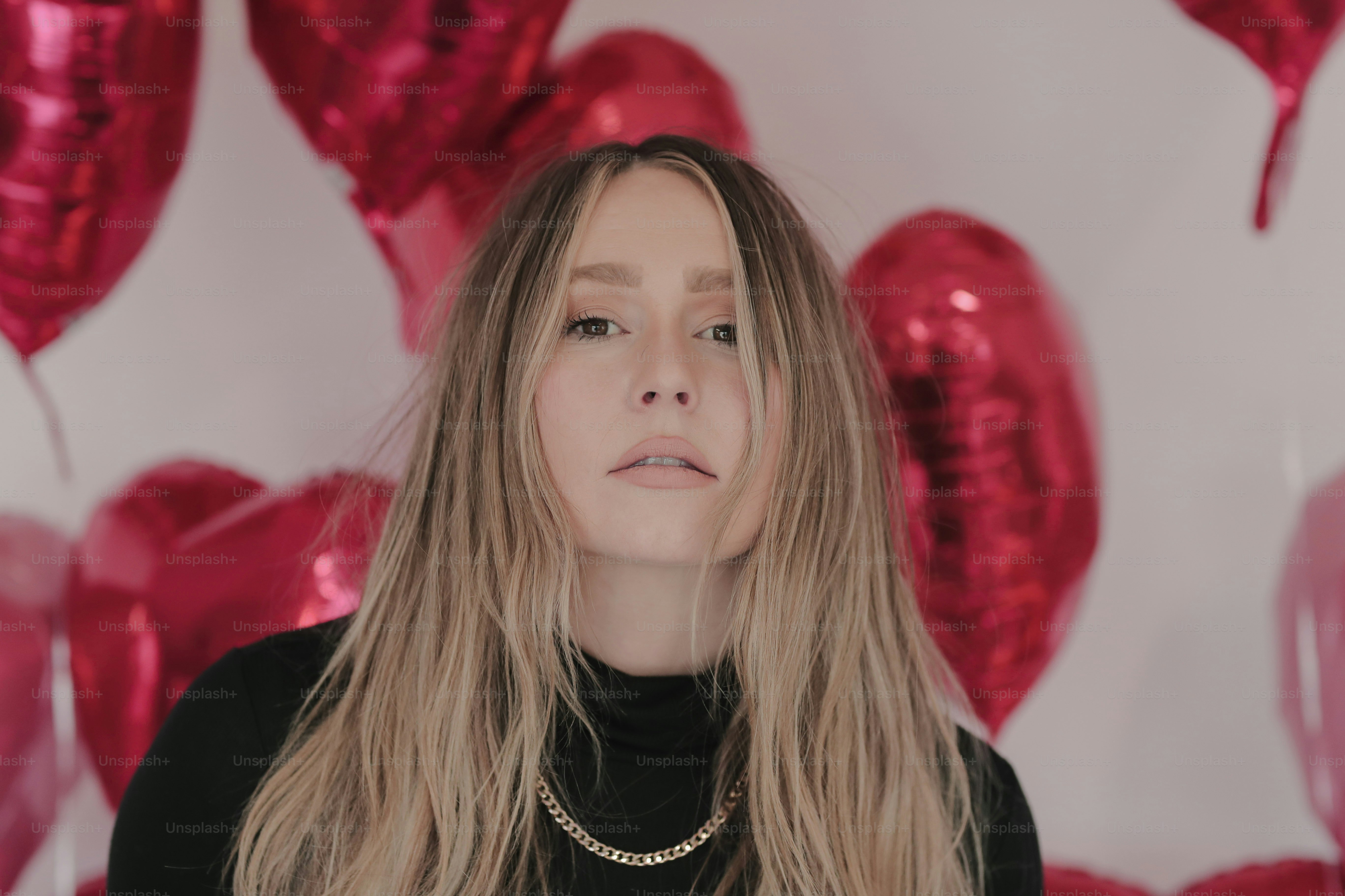 a woman with long blonde hair standing in front of heart shaped balloons