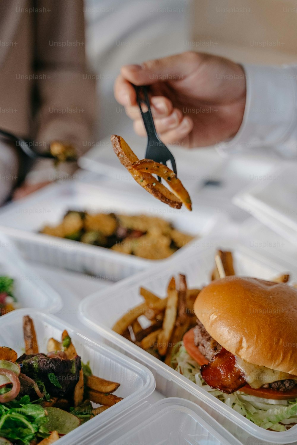 a person holding a fork over a hamburger and french fries