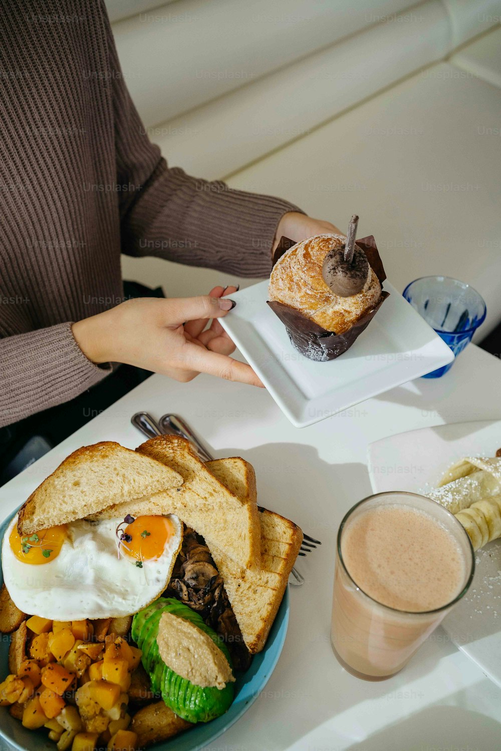 Una persona sosteniendo un plato con un sándwich y una taza de café
