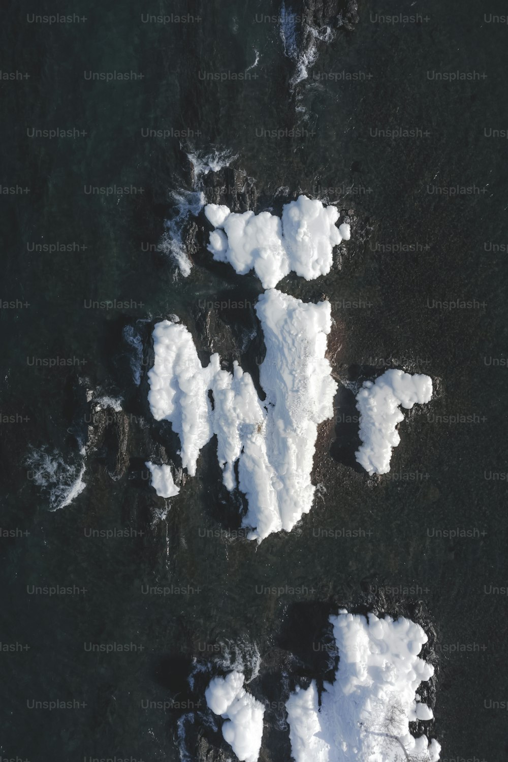 an aerial view of snow covered rocks in the water