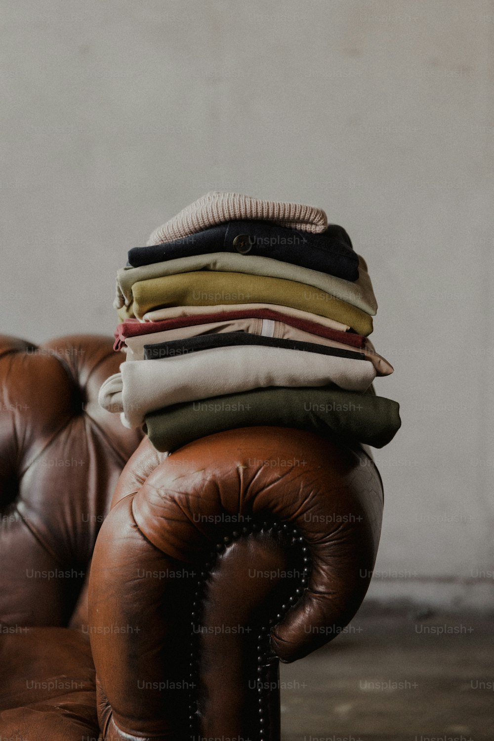 a pile of folded clothes sitting on top of a brown leather chair