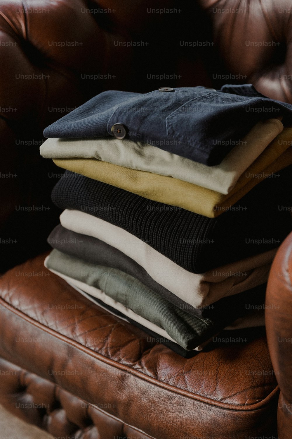 uma pilha de roupas dobradas sentada em cima de uma cadeira de couro marrom