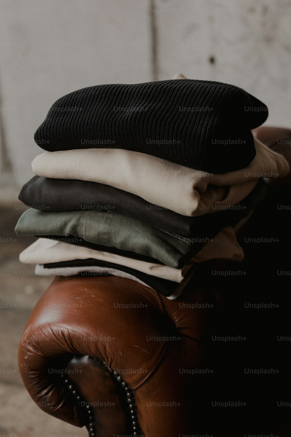uma pilha de roupas dobradas sentada em cima de uma cadeira de couro