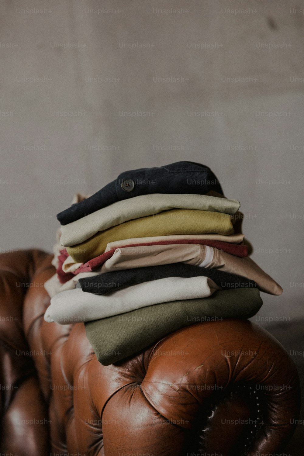 a pile of clothes sitting on top of a brown leather chair