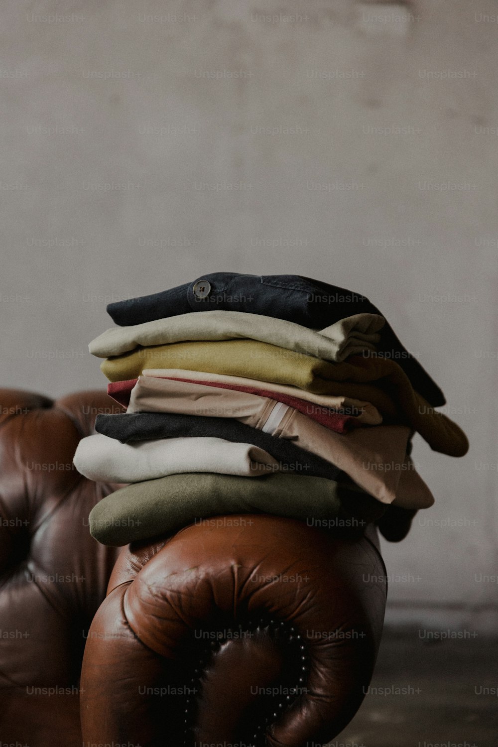 a pile of clothes sitting on top of a brown leather chair