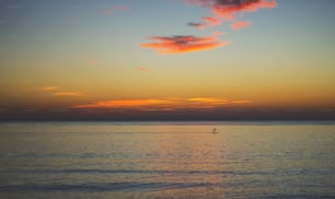 a lone boat in the middle of the ocean at sunset