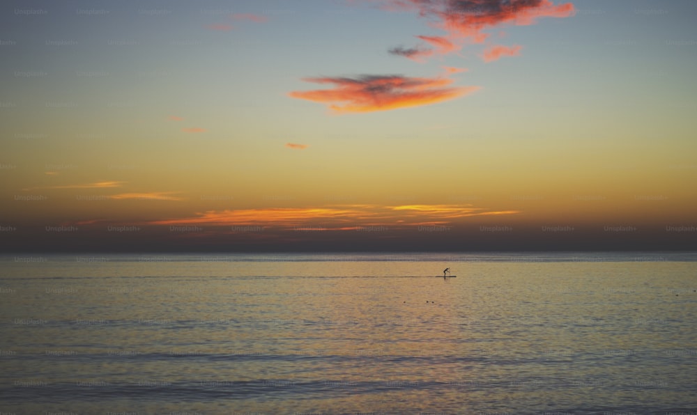 a lone boat in the middle of the ocean at sunset