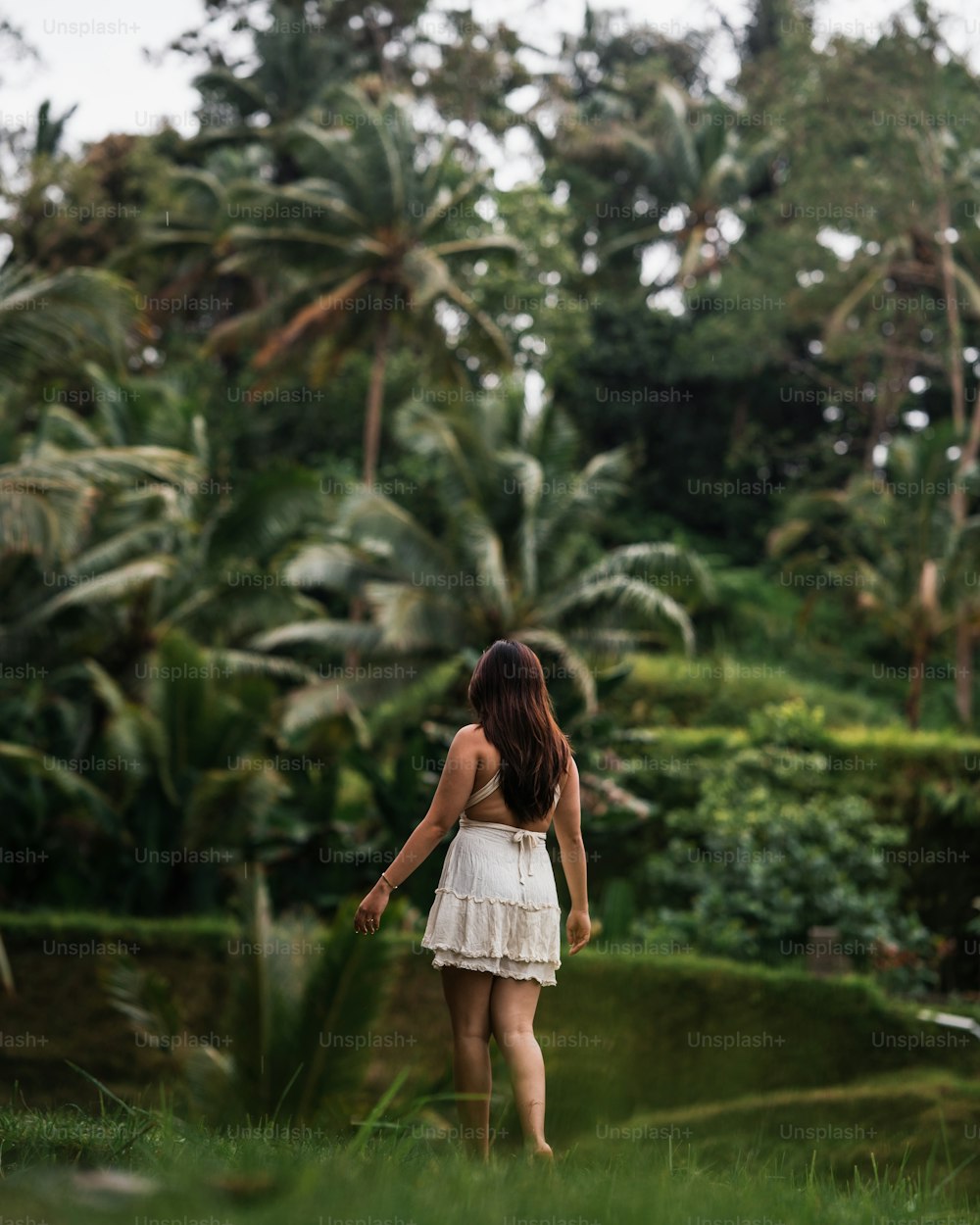 a woman in a white dress walking through a lush green forest