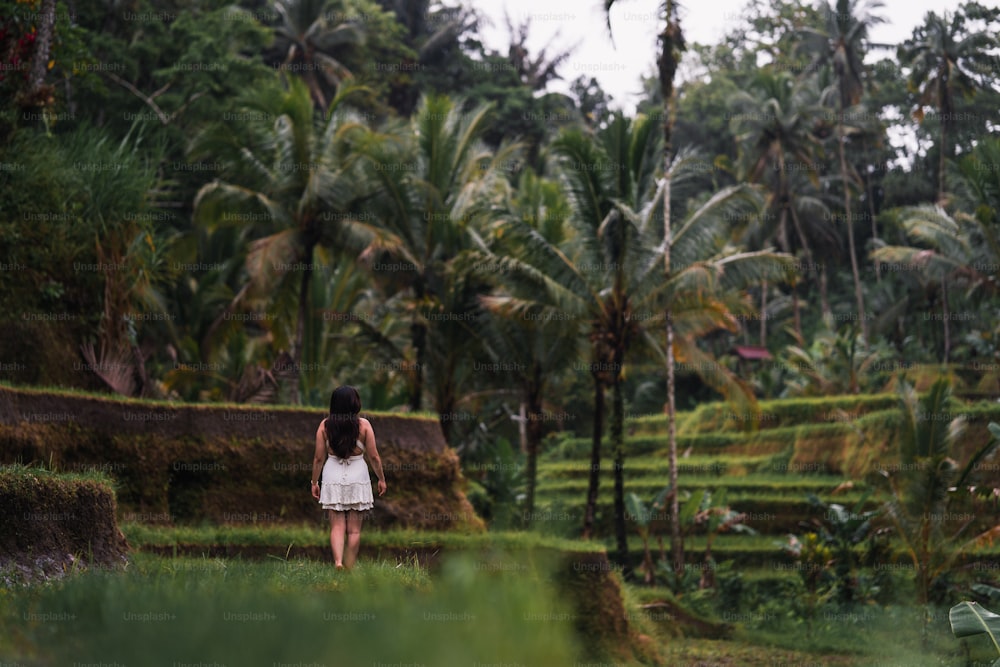 a woman in a white dress walking through a lush green field