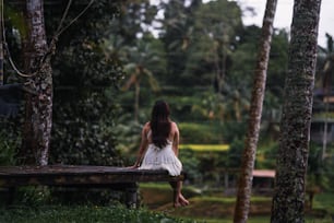 a woman sitting on a wooden bench in a forest