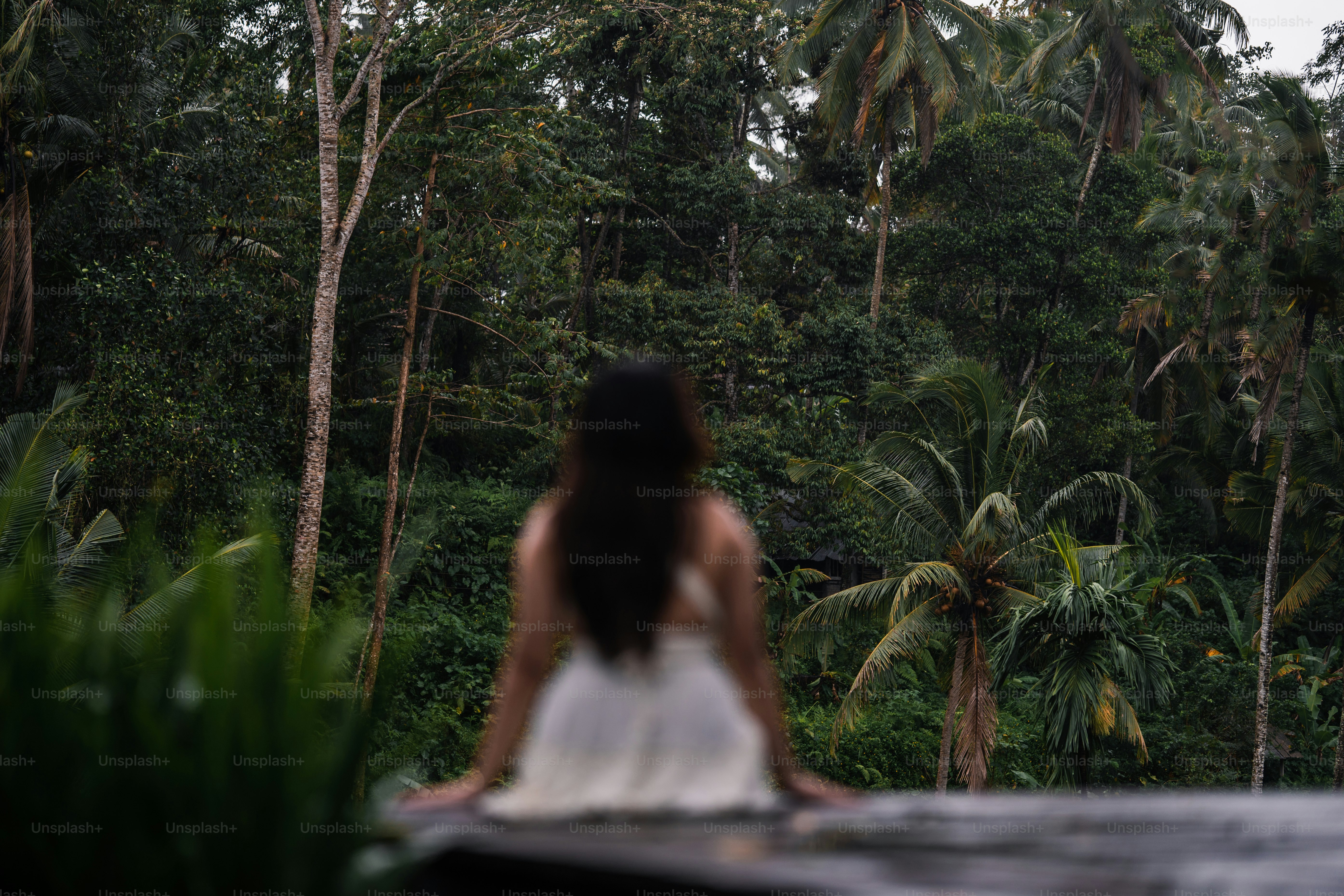 Seorang wanita bergaun putih berdiri di depan hutan