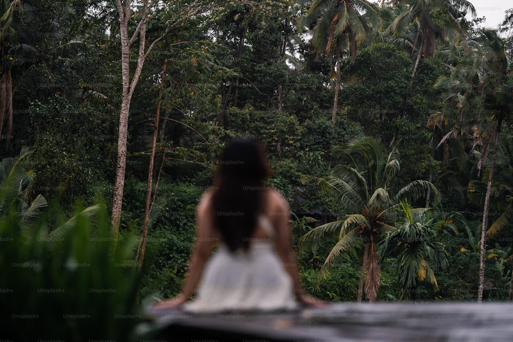 uma mulher em um vestido branco em pé na frente de uma floresta
