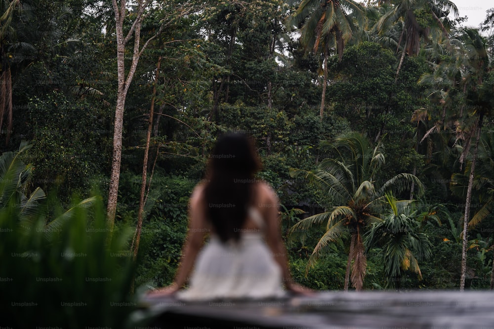 a woman in a white dress standing in front of a forest