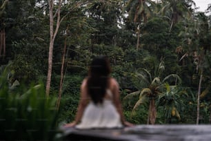 a woman in a white dress standing in front of a forest