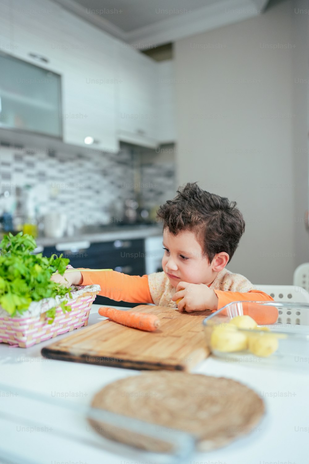 a little boy sitting at a table with a basket of vegetables