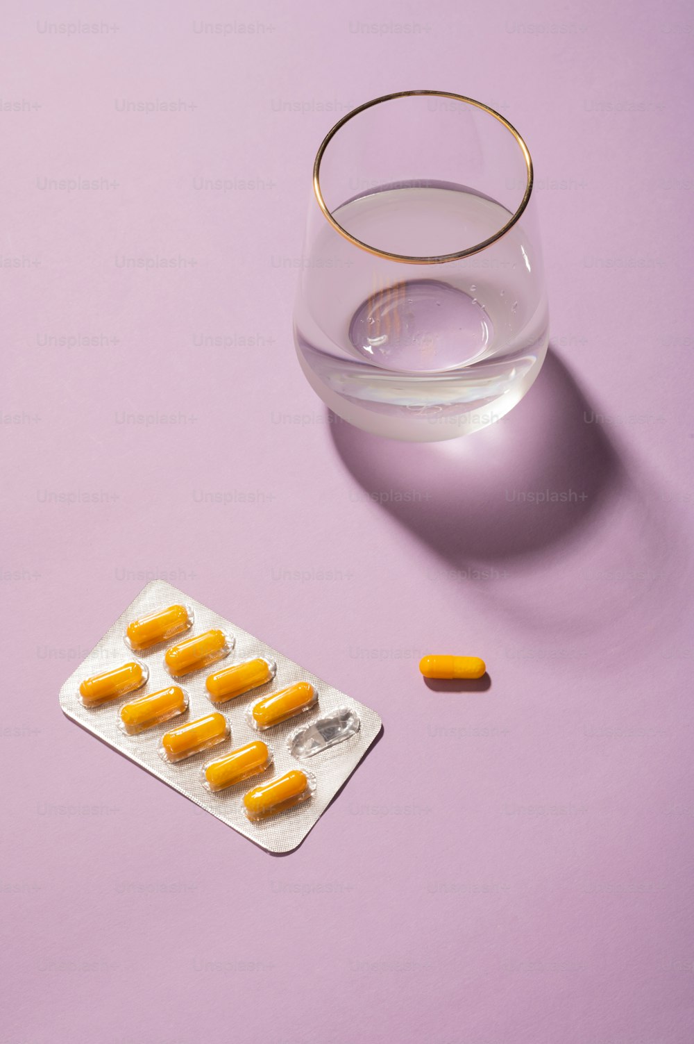 pills and a glass of water on a purple surface