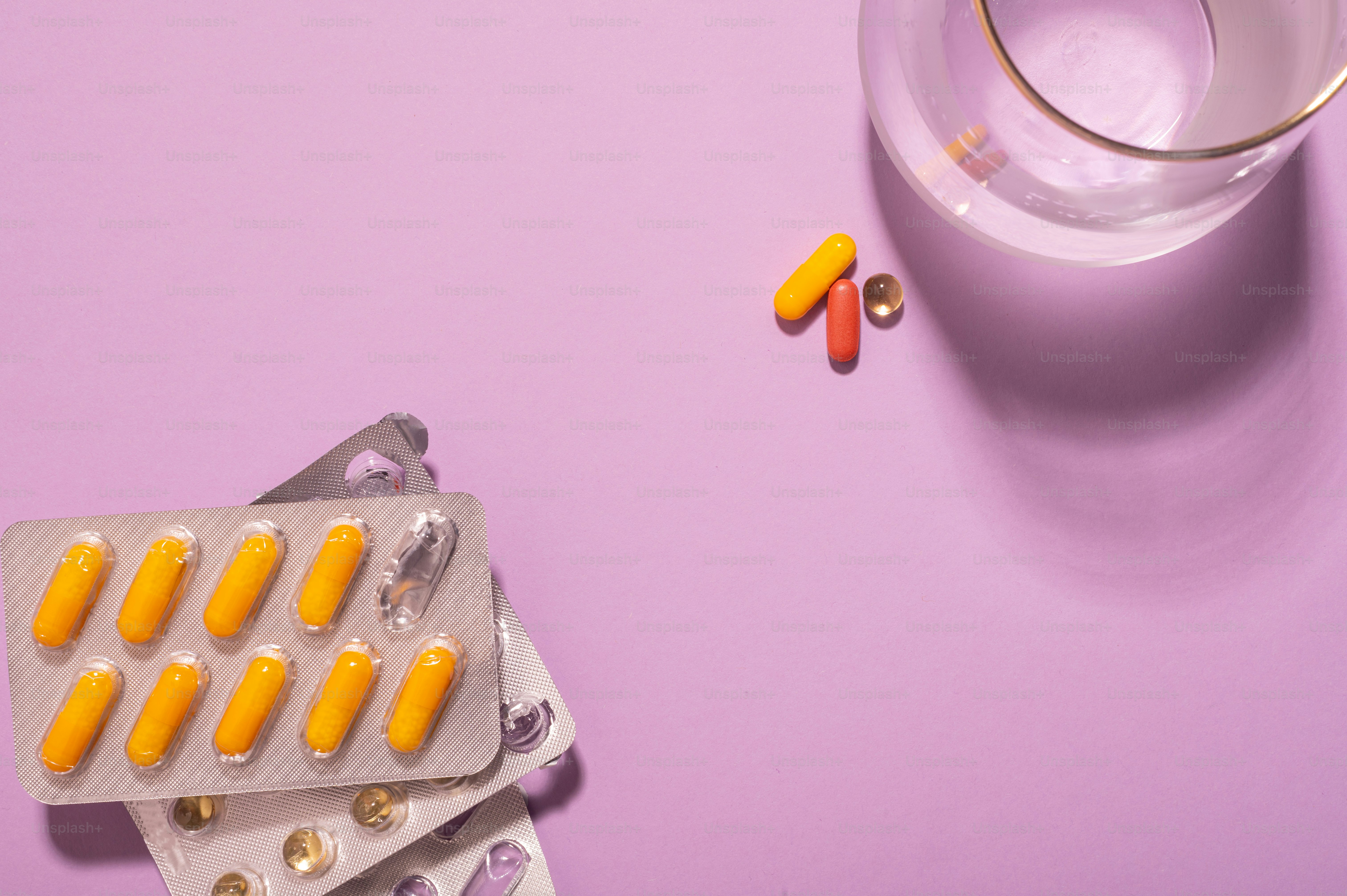 pillole e un bicchiere d'acqua su una superficie viola