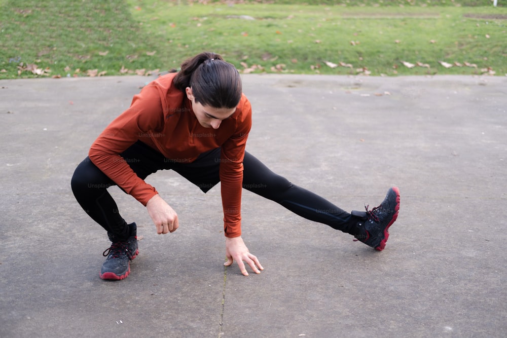 a woman in a red shirt and black leggings bends down to pick up