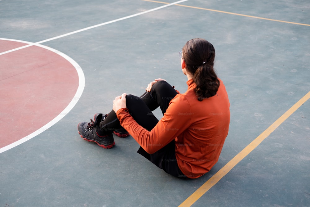 a woman sitting on a basketball court with her legs crossed