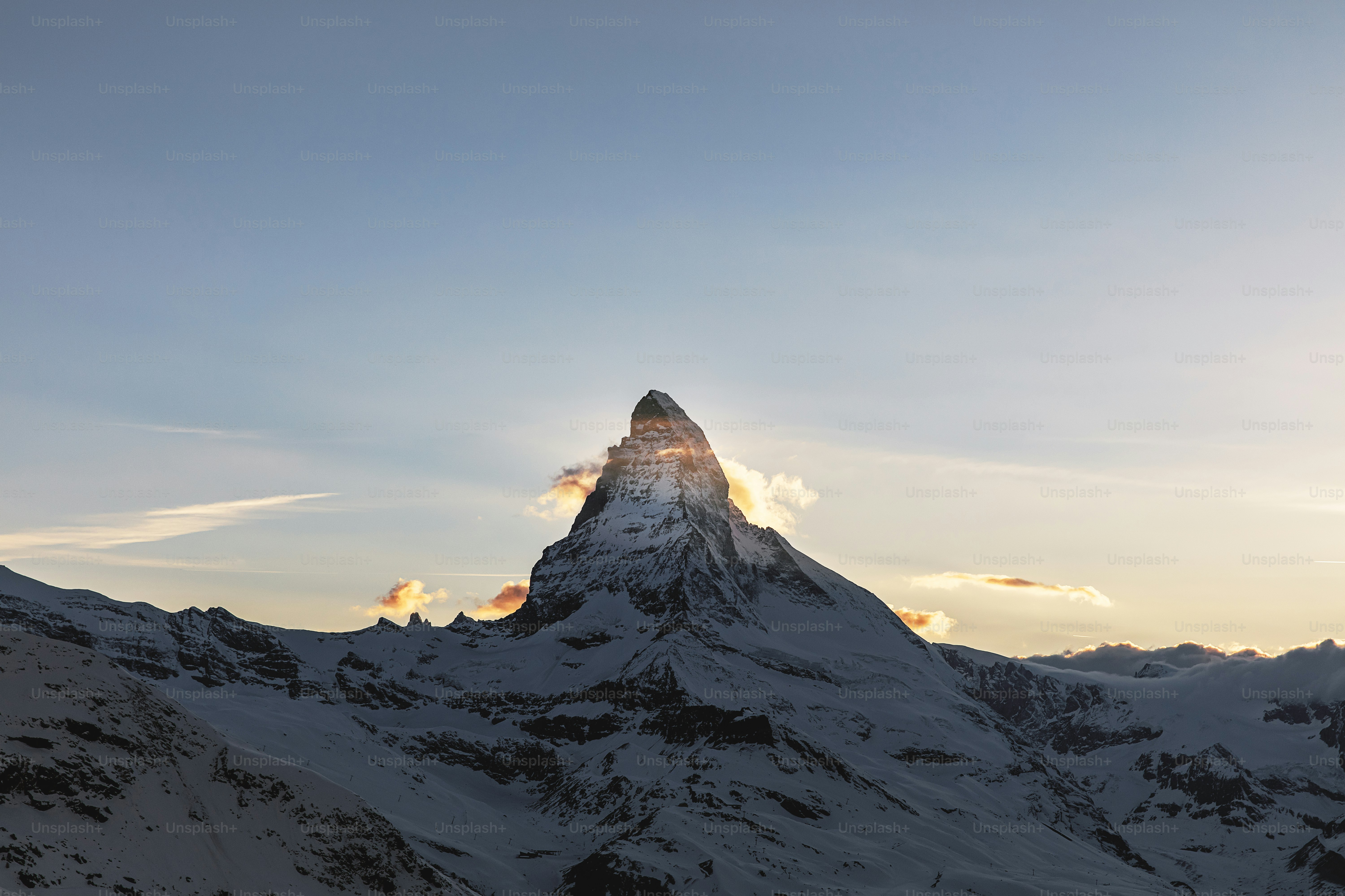 Una montaña cubierta de nieve con el sol asomándose a través de las nubes