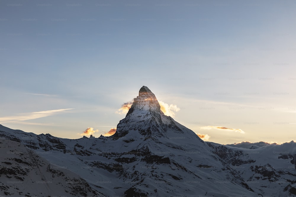 uma montanha coberta de neve com o sol espreitando através das nuvens