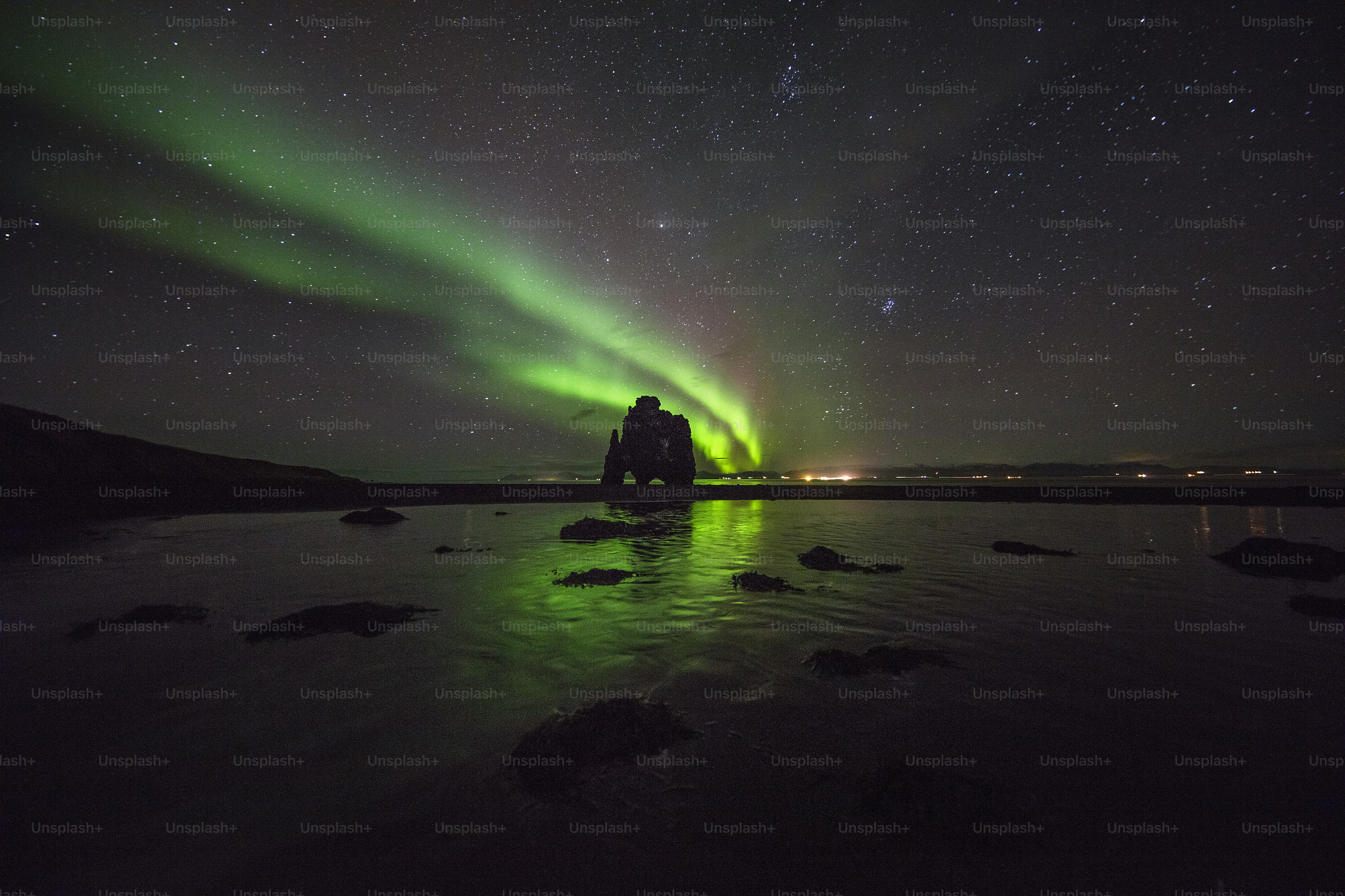 Una persona parada en una roca en el agua bajo una aurora verde y azul