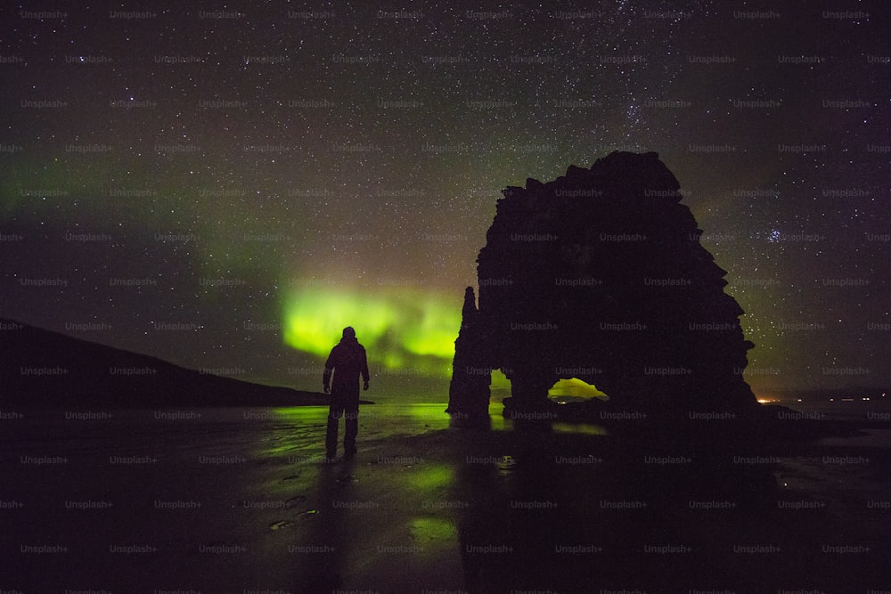 a man standing on a beach under a green and purple sky