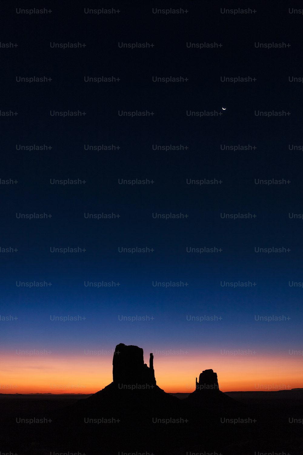 the moon is setting over the desert with a rock formation in the foreground