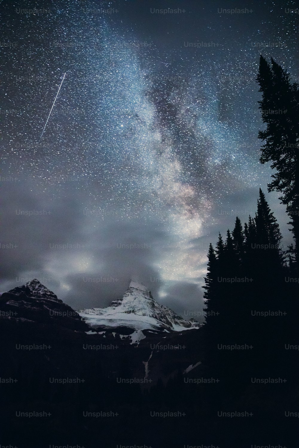 a night sky with a mountain and trees in the foreground